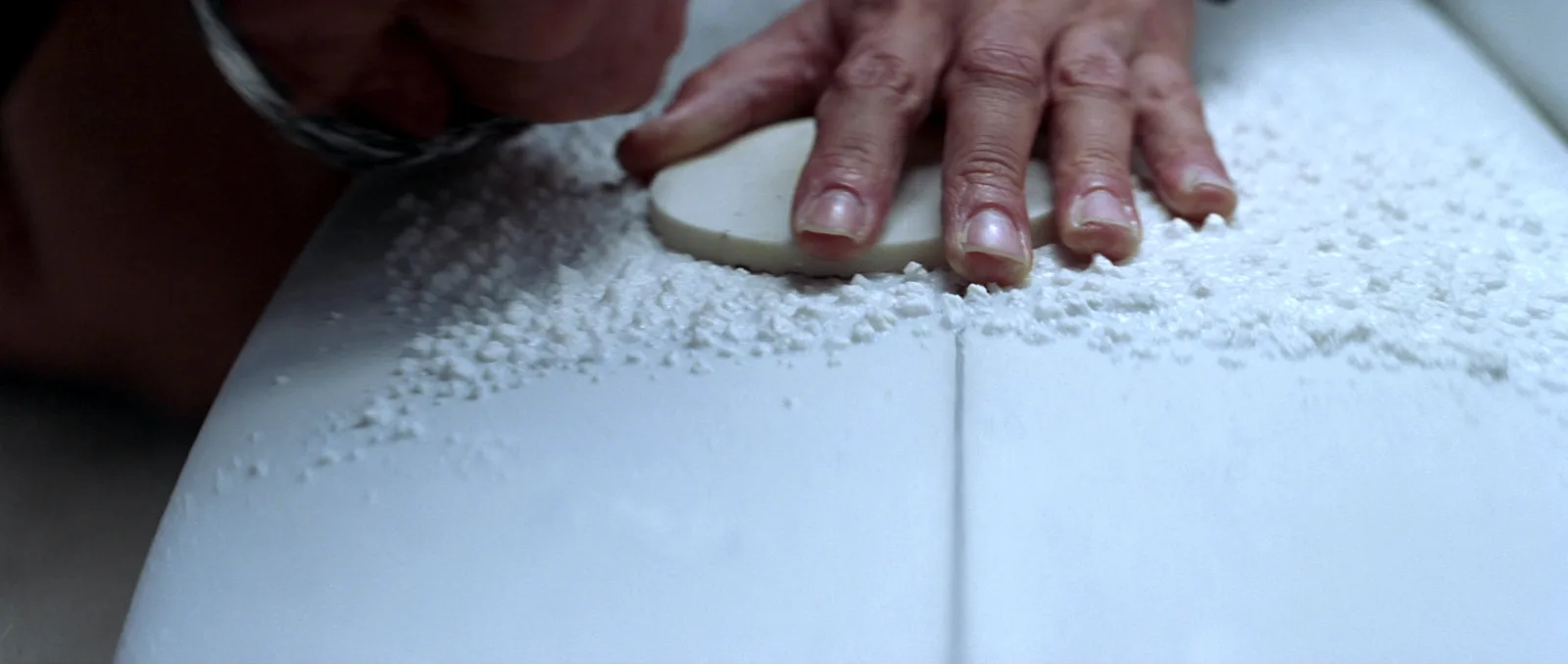 How to wax a surfboard — hands rubbing a bar of surf wax into the deck, wax bumps forming