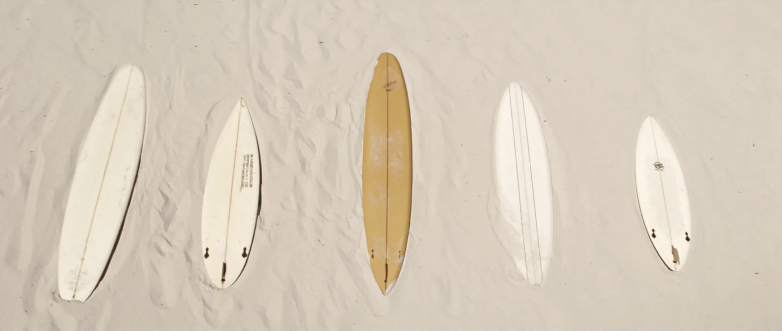 Surfboard size chart — five surfboards of different lengths laid out side by side on the sand