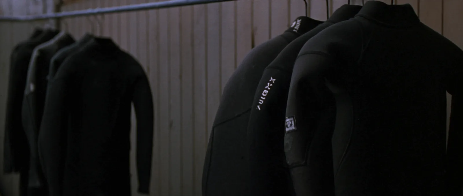 Wetsuit size chart — a row of neoprene wetsuits in different sizes hanging up to dry